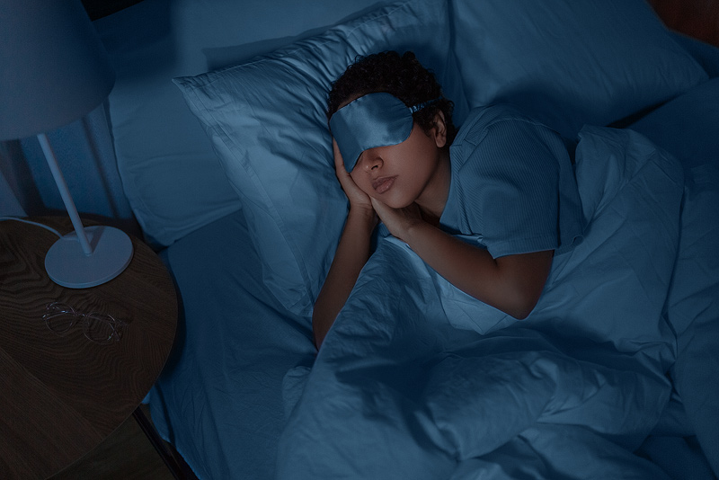 Een vrouw ligt in een uitnodigend bed met een slaapmasker op.