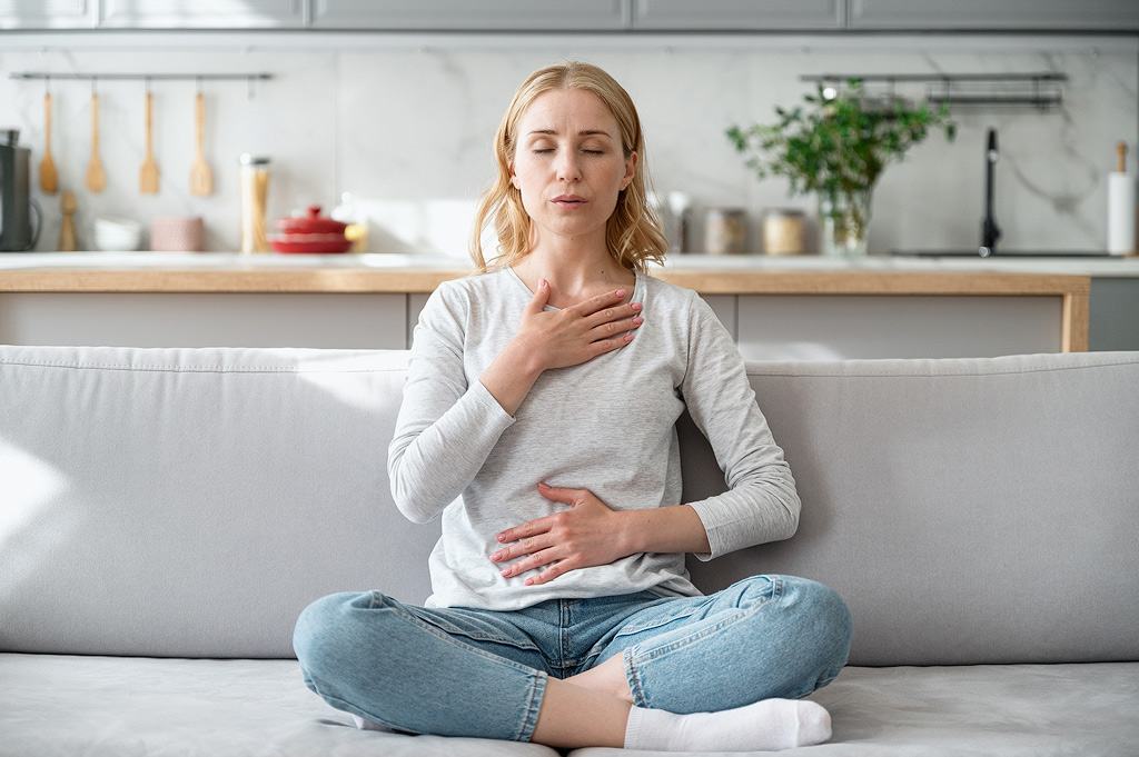 Een vrouw voelt haar ademhaling tijdens een meditatie op de bank in een open keuken.