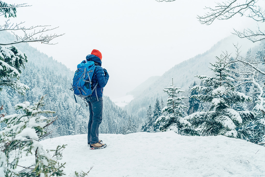 Een vrouw in outdoor kleding kijkt uit over een winters landschap.